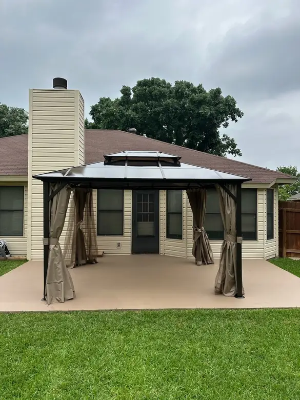 Hardtop gazebo with drapes installed on a patio behind a house