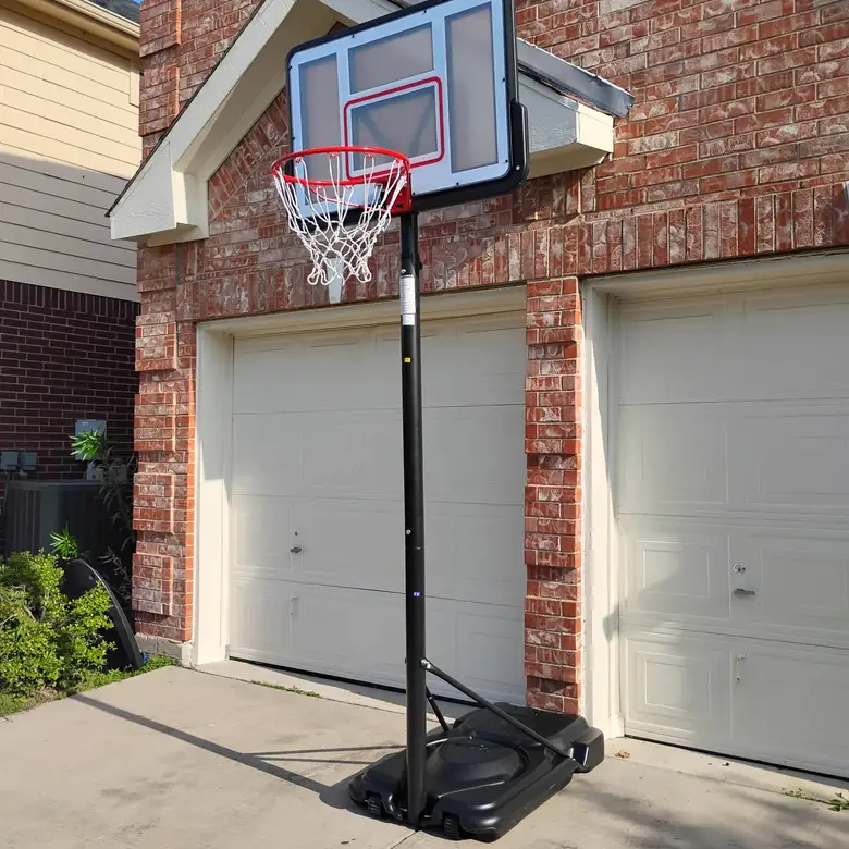 Portable basketball hoop assembled on a driveway in front of a brick house