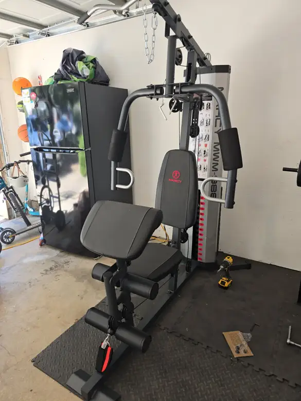 Multi-station home gym with a bench assembled in a garage