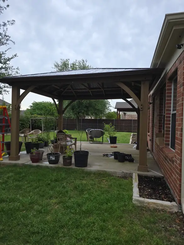 Cedar pavilion built over a back patio beside a brick house