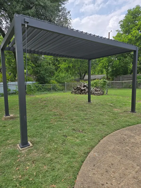 Black aluminium pergola standing on a lawn beside a driveway