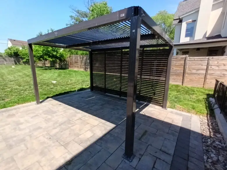 Louvered pergola with a privacy wall installed over a paver patio