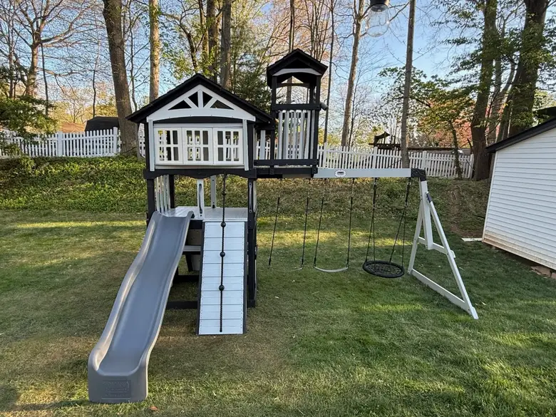 Wooden playset fort with a slide and swing set installed on a lawn