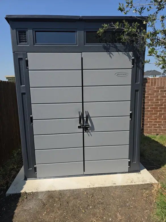 Resin storage shed assembled and levelled beside a fence