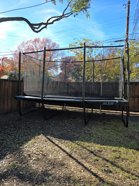 Rectangular trampoline with a safety net assembled in a fenced back yard